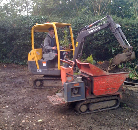 A mini digger loading soil into a tracked dumper.